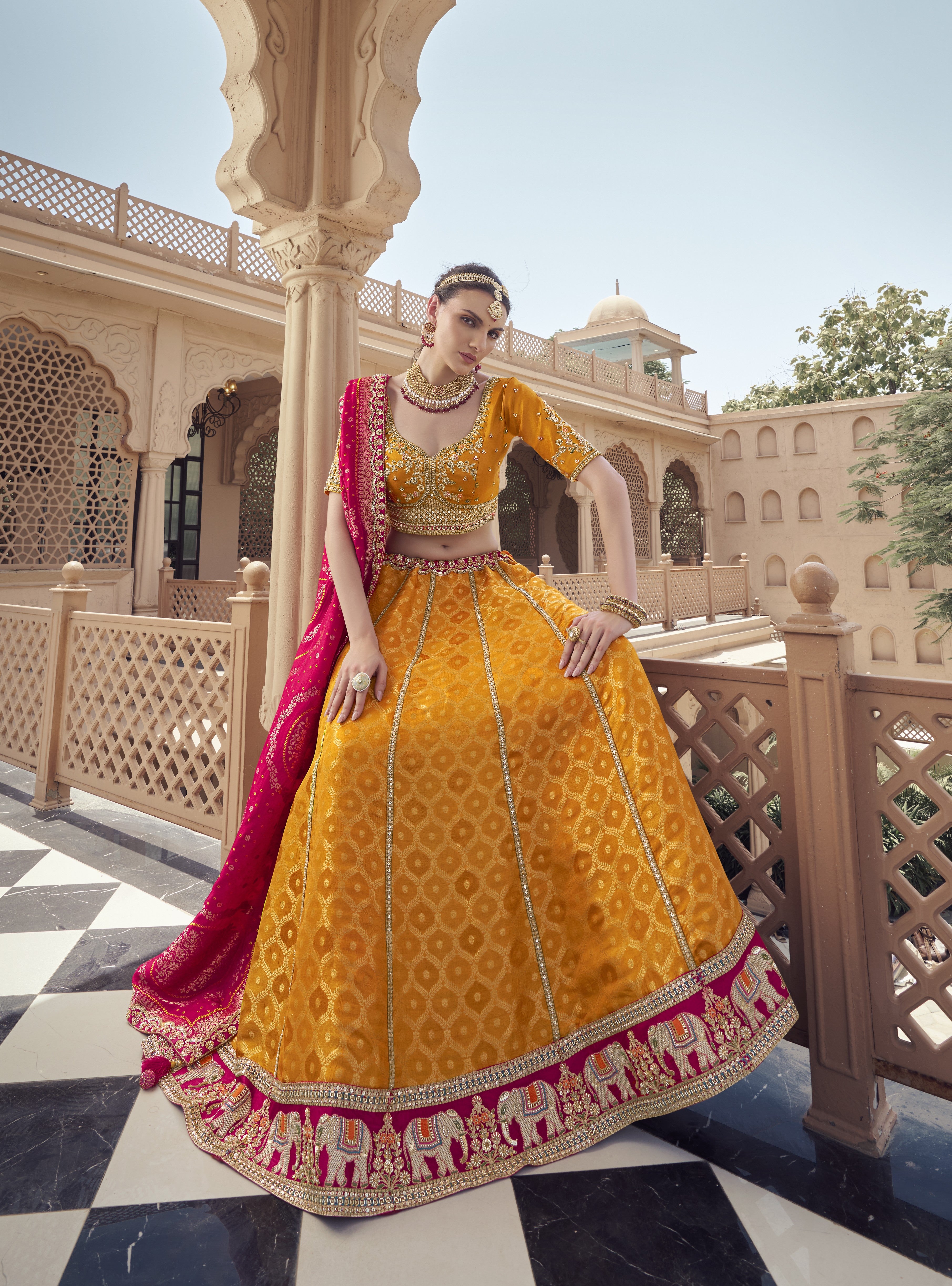 Woman in traditional yellow and pink embroidered Lehenga with jewelry outdoors.