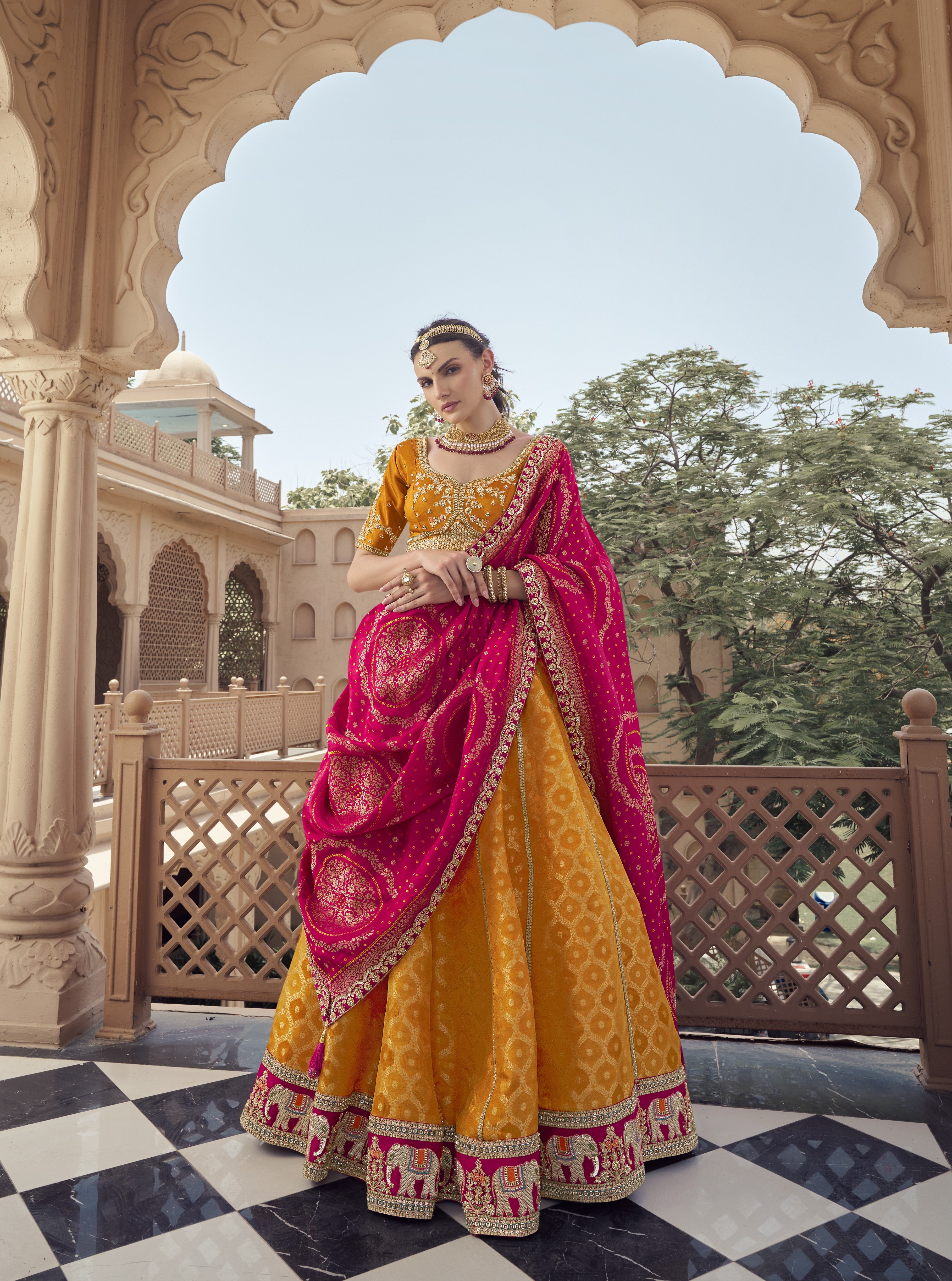 Woman in traditional yellow and pink embroidered Lehenga with jewelry outdoors.