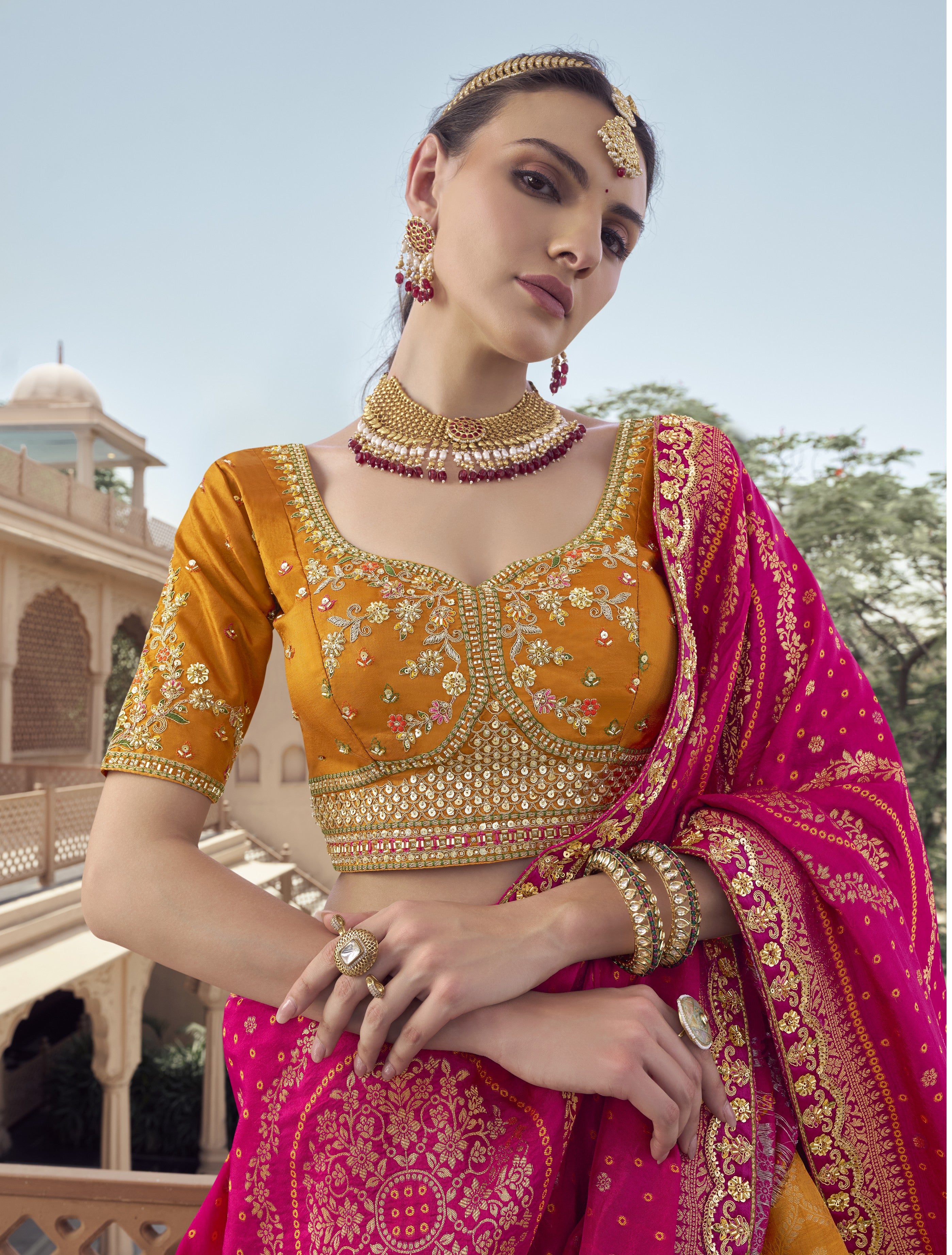Woman in traditional yellow and pink embroidered Lehenga with jewelry outdoors.