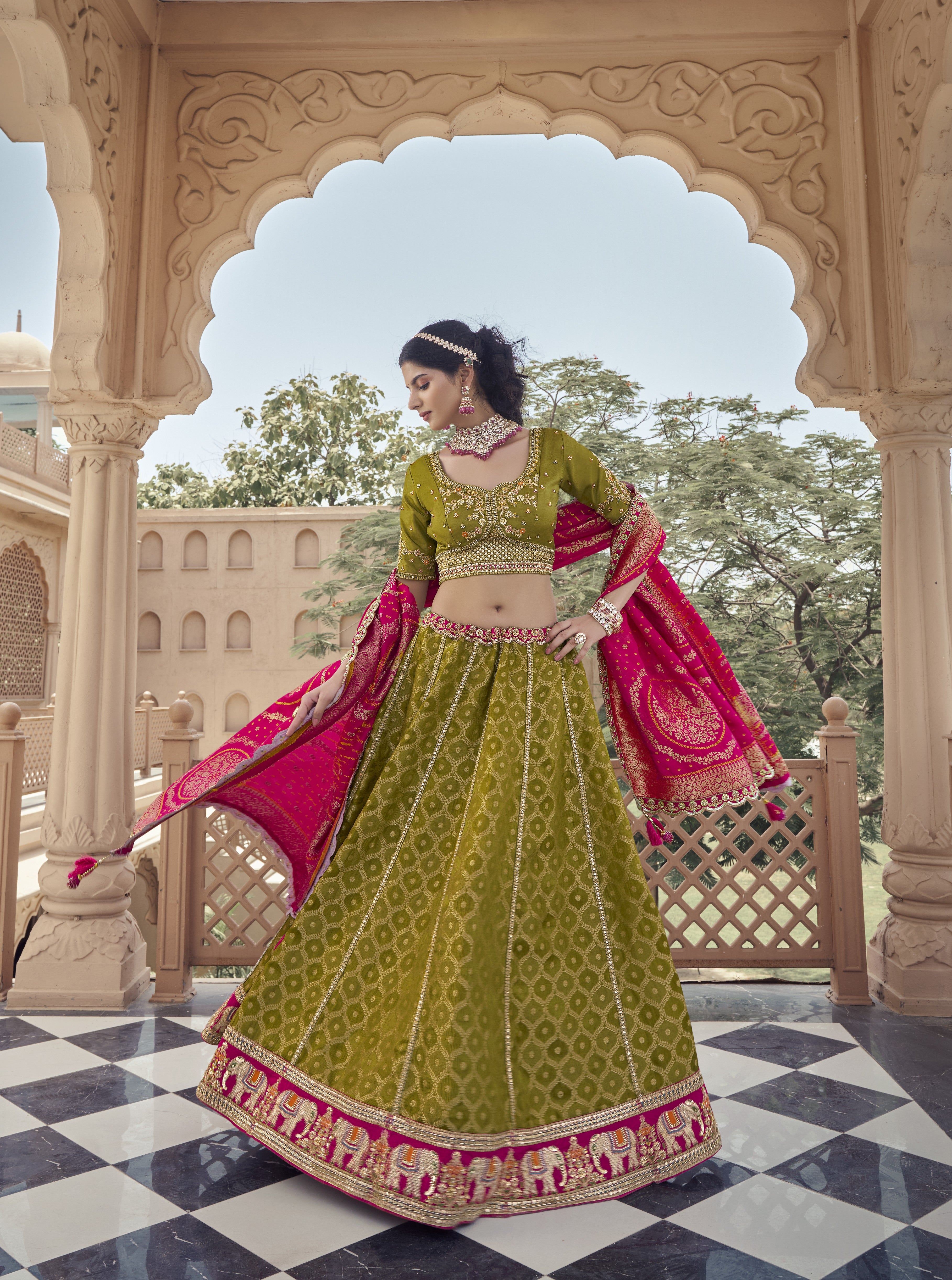 Woman in a green and pink traditional outfit standing in front of an ornate archway.