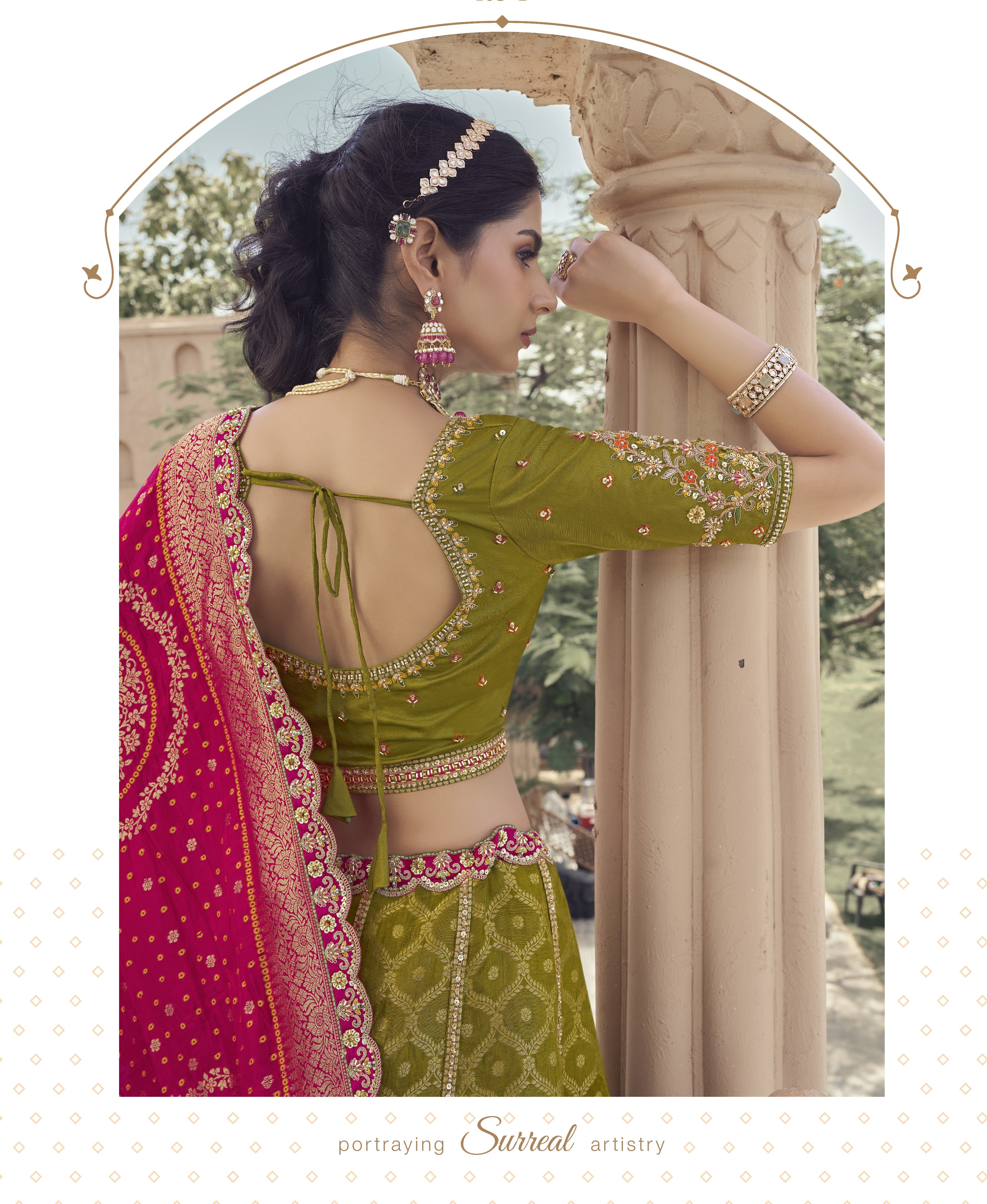 Woman in a green and pink traditional outfit with jewelry, standing in a scenic outdoor setting.